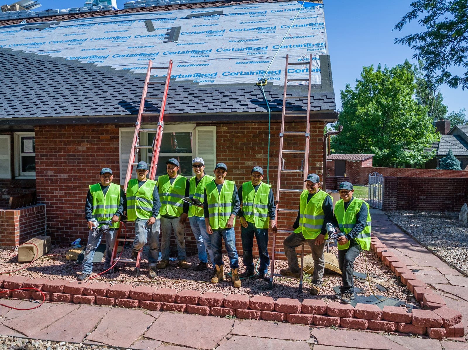 The Foothills crew in hi-vis vests in front of a brick home mid re-roof